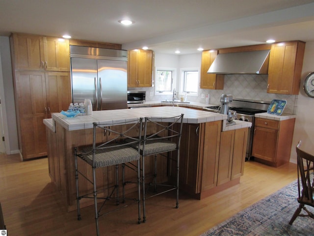2011 Douglas Dr, Tawas City, MI 48763 - kitchen with exhaust hood, tile counters, stainless steel appliances, a center island, and light wood-style flooring