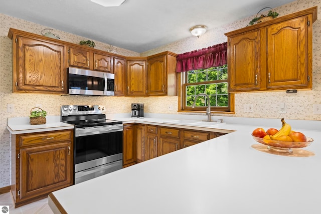 11103 S Ramblewood Dr, Cedar, MI 49621 - kitchen featuring stainless steel appliances, wallpapered walls, a sink, light countertops, and brown cabinets