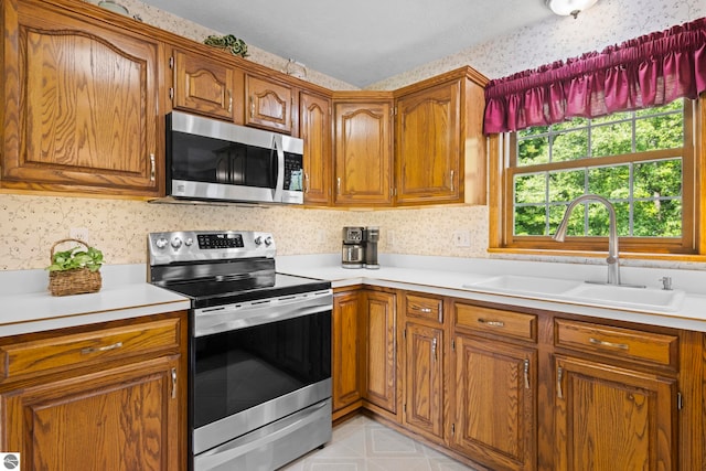 11103 S Ramblewood Dr, Cedar, MI 49621 - kitchen featuring stainless steel appliances, a sink, wallpapered walls, brown cabinets, and light countertops