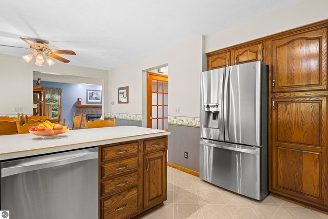 11103 S Ramblewood Dr, Cedar, MI 49621 - kitchen featuring appliances with stainless steel finishes, a brick fireplace, light countertops, brown cabinets, and light flooring