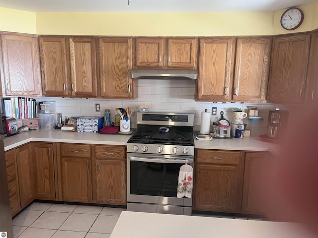 2168 S Lorenz Rd, Tawas City, MI 48763 - kitchen with stainless steel range with gas stovetop, exhaust hood, light tile patterned floors, light countertops, and brown cabinetry