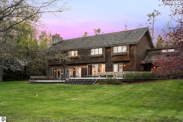 12150 N Seven Pines Rd, Northport, MI 49670 - back of house at dusk with a yard, a chimney, and a deck