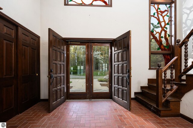 12150 N Seven Pines Rd, Northport, MI 49670 - entrance foyer featuring brick flooring, baseboards, stairway, french doors, and a towering ceiling