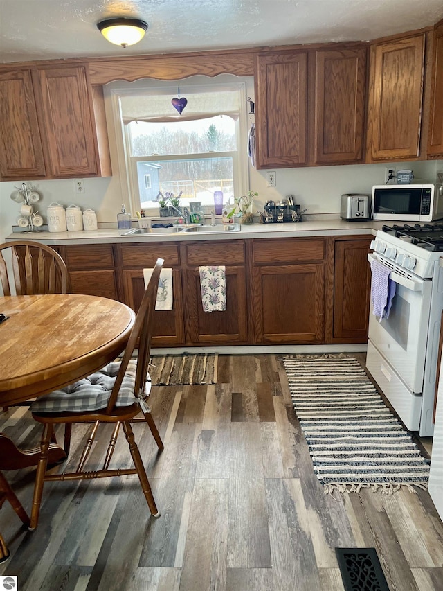 7813 Standish Rd, Bentley, MI 48613 - kitchen with white range with gas stovetop, stainless steel microwave, dark wood-style flooring, brown cabinets, and light countertops