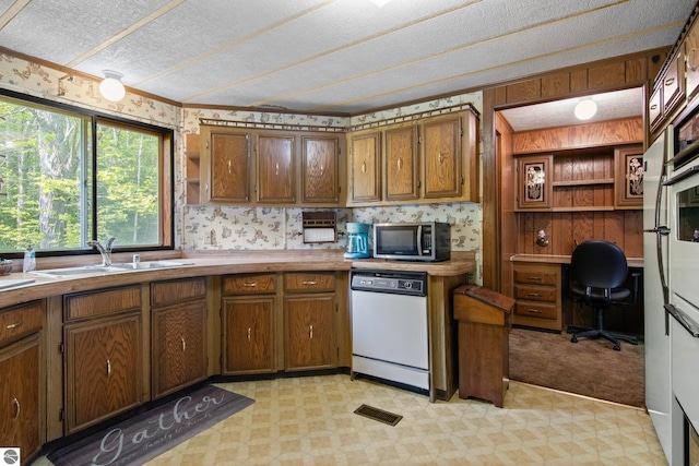 14501 Williams Dr, Elk Rapids, MI 49629 - kitchen featuring dishwasher, stainless steel microwave, light floors, brown cabinetry, and a sink