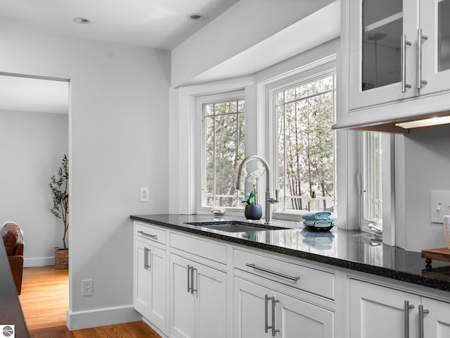 107 Hillcrest Ct, Traverse City, MI 49684 - kitchen with dark stone counters, white cabinetry, a sink, wood finished floors, and glass insert cabinets