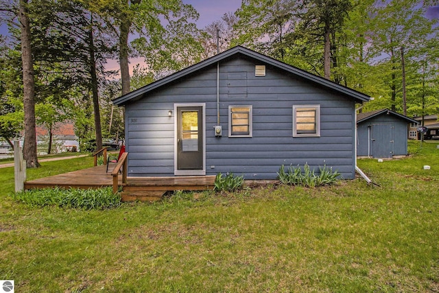 3131 Herron Rd, Frankfort, MI 49635 - back of property at dusk featuring a deck, a lawn, and an outbuilding