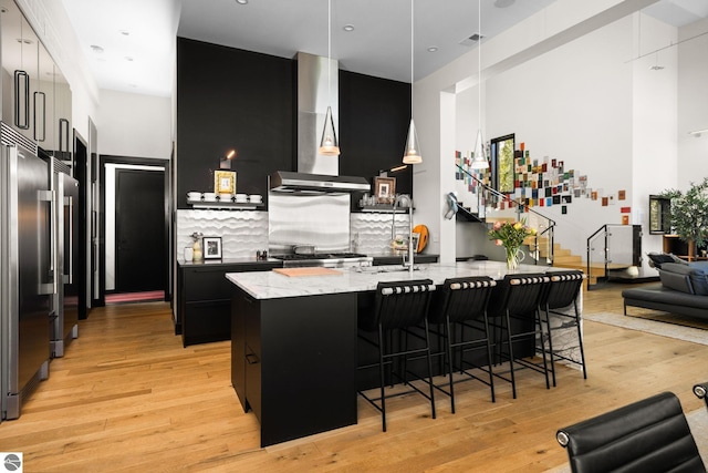 9371 Onominese Trl, Northport, MI 49670 - kitchen featuring wall chimney range hood, dark cabinetry, a breakfast bar, stainless steel built in fridge, and light wood-type flooring