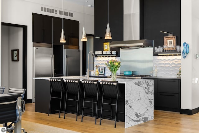 9371 Onominese Trl, Northport, MI 49670 - kitchen featuring wall chimney exhaust hood, dark cabinetry, high end fridge, and light wood-style flooring