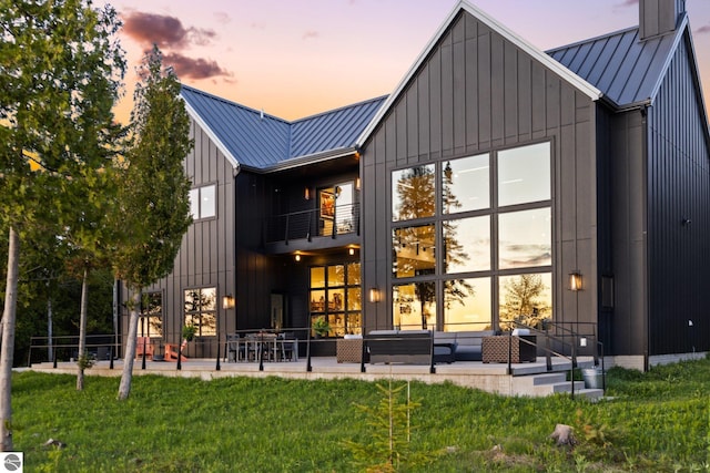 9371 Onominese Trl, Northport, MI 49670 - back of house at dusk with a balcony, a standing seam roof, metal roof, a lawn, and a patio area