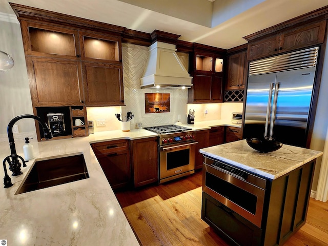 5707 S Lake St Unit 13F, Glen Arbor, MI 49636 - kitchen with high quality appliances, custom exhaust hood, a sink, tasteful backsplash, and light wood finished floors