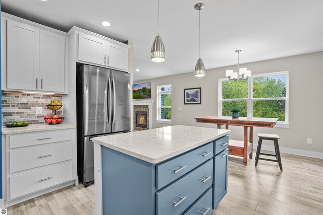 9207 Mockingbird Ln, Cadillac, MI 49601 - kitchen with freestanding refrigerator, white cabinets, a center island, decorative backsplash, and pendant lighting