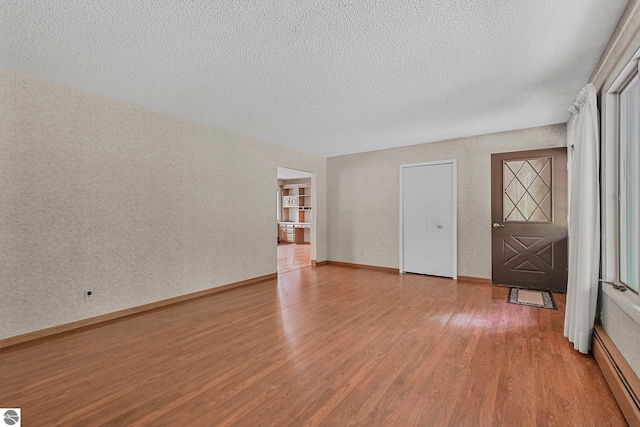 9017 Clam Lake Rd, Bellaire, MI 49615 - unfurnished living room featuring baseboard heating, wood finished floors, a textured ceiling, and baseboards