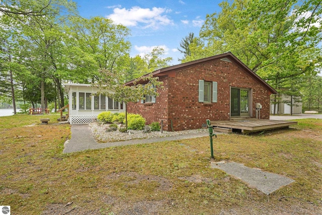 9017 Clam Lake Rd, Bellaire, MI 49615 - view of home's exterior featuring a sunroom, a wooden deck, brick siding, and a lawn