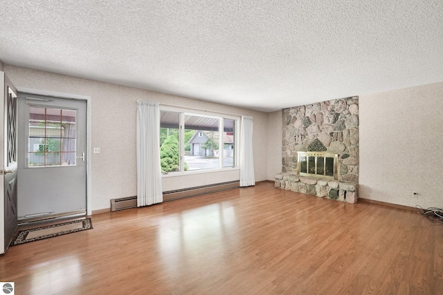 9017 Clam Lake Rd, Bellaire, MI 49615 - unfurnished living room featuring wood finished floors, a textured ceiling, a fireplace, a baseboard heating unit, and baseboards