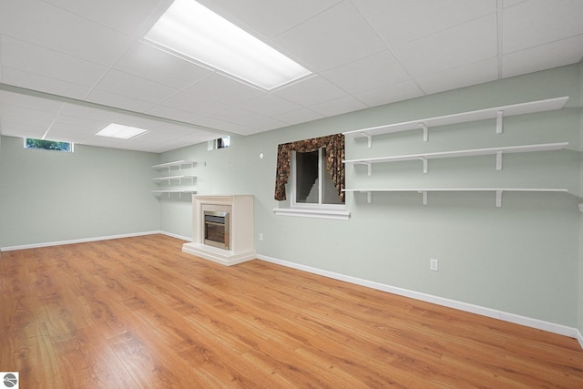 9017 Clam Lake Rd, Bellaire, MI 49615 - unfurnished living room featuring a glass covered fireplace, light wood finished floors, a paneled ceiling, and baseboards