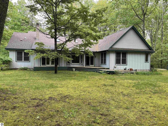 5867 Huron Woods Dr, Tawas City, MI 48763 - rear view of house featuring board and batten siding, a yard, a chimney, and a shingled roof