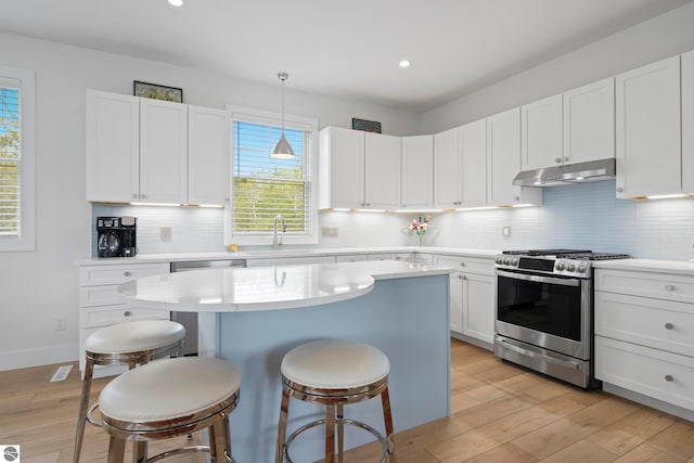 5896 S Cummings St, Suttons Bay, MI 49682 - kitchen featuring appliances with stainless steel finishes, under cabinet range hood, a sink, a kitchen breakfast bar, and light wood-style flooring