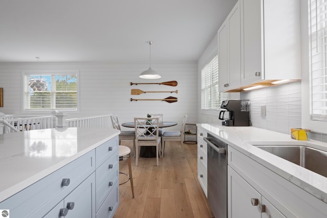 5896 S Cummings St, Suttons Bay, MI 49682 - kitchen with stainless steel dishwasher, light wood-style floors, white cabinets, hanging light fixtures, and light stone countertops