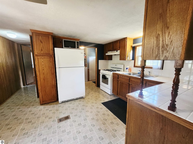 3764 E N Down River Rd, Grayling, MI 49738 - kitchen with white appliances, tile countertops, a sink, under cabinet range hood, and brown cabinetry