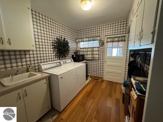 739 Stimson St, Cadillac, MI 49601 - laundry area featuring wallpapered walls, separate washer and dryer, wood finished floors, and cabinet space