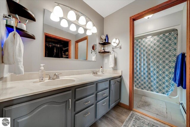 6369 Wooded Trl, Houghton Lake, MI 48629 - bathroom featuring double vanity, curtained shower, a baseboard heating unit, wood finished floors, and a walk in closet