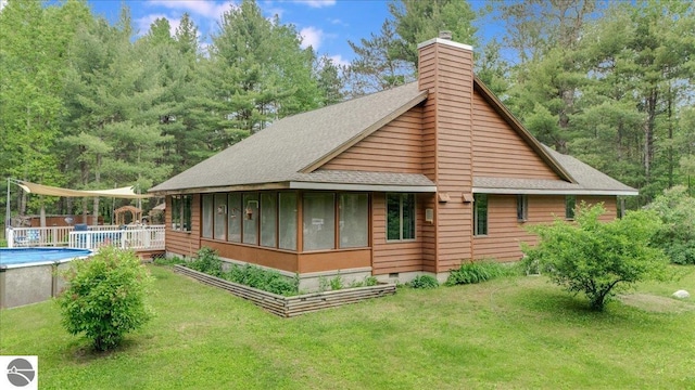 6369 Wooded Trl, Houghton Lake, MI 48629 - back of property with roof with shingles, a chimney, a sunroom, a yard, and an outdoor pool
