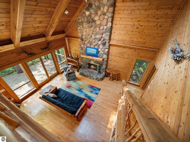 10037 Mud Lake Rd, Interlochen, MI 49643 - living room with a wood ceiling with exposed beams, wood finished floors, wooden walls, a stone fireplace, and high vaulted ceiling