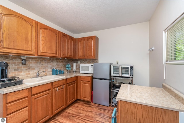 7373 Blue Ox Trl, South Branch, MI 48761 - kitchen with white microwave, freestanding refrigerator, light wood-type flooring, light countertops, and backsplash
