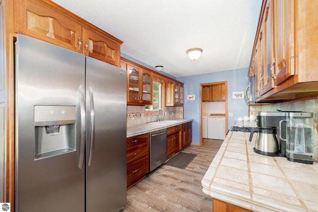 7746 Five Lakes Dr, Farwell, MI 48622 - kitchen with stainless steel appliances, tile counters, washer and dryer, light wood-style floors, and decorative backsplash