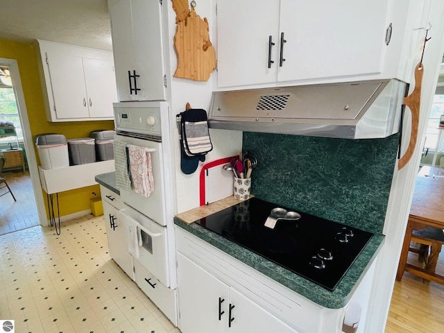 801 N Bridge St, Bellaire, MI 49615 - kitchen featuring black electric stovetop, white oven, white cabinetry, exhaust hood, and light flooring
