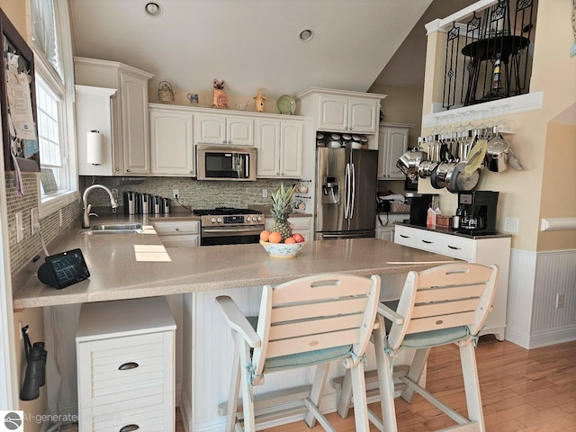 1005 W Lake St Unit 4, Tawas City, MI 48763 - kitchen with stainless steel appliances, a peninsula, tasteful backsplash, light wood-type flooring, and a kitchen bar