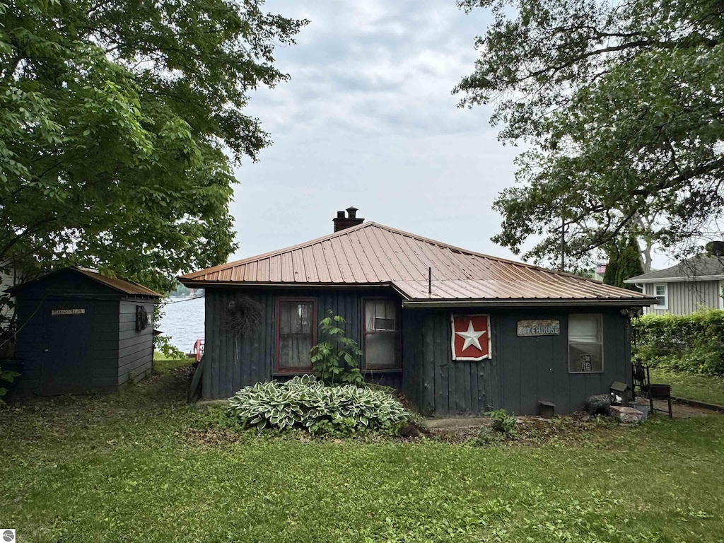 1271 N Crooked Lake Dr, Lake, MI 48632 - view of property exterior featuring a chimney, a yard, board and batten siding, a metal roof, and a storage unit