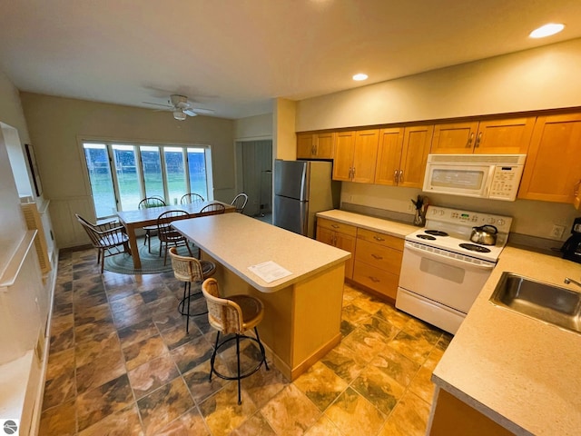 407 S Main St, Leland, MI 49654 - kitchen featuring white appliances, a kitchen bar, a ceiling fan, light countertops, and brown cabinetry