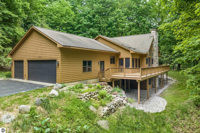 6352 S Westwood Pkwy, Suttons Bay, MI 49682 - view of front of home with a wooden deck, a chimney, roof with shingles, a detached garage, and a front lawn