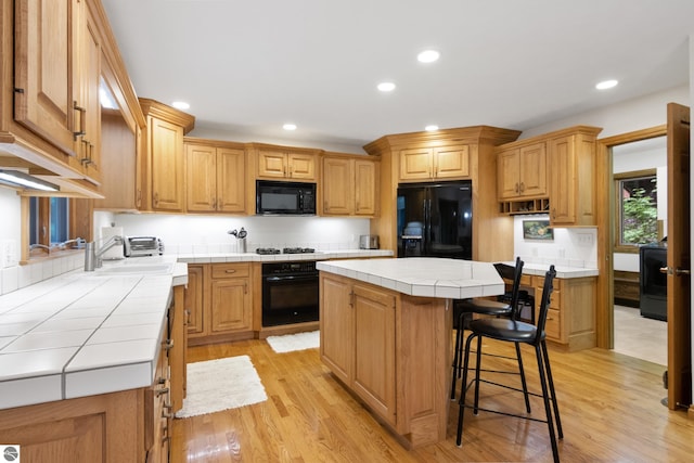 6352 S Westwood Pkwy, Suttons Bay, MI 49682 - kitchen featuring black appliances, tile counters, light wood finished floors, a center island, and recessed lighting
