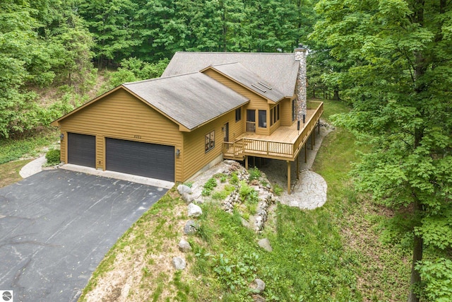 6352 S Westwood Pkwy, Suttons Bay, MI 49682 - rustic home featuring asphalt driveway, a deck, a chimney, roof with shingles, and an attached garage