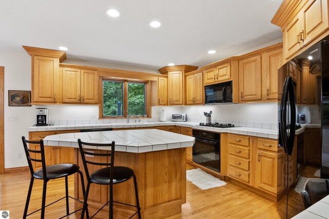 6352 S Westwood Pkwy, Suttons Bay, MI 49682 - kitchen with black appliances, tile counters, a center island, a breakfast bar, and light wood-style floors