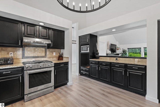 1259 Lin Dale Dr, Traverse City, MI 49686 - kitchen featuring appliances with stainless steel finishes, dark cabinetry, under cabinet range hood, vaulted ceiling, and light wood-type flooring