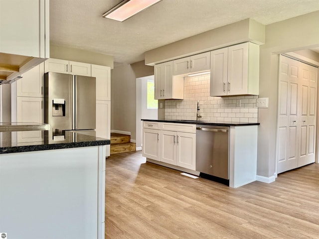 7160 Cherry Ave, Kewadin, MI 49648 - kitchen featuring stainless steel appliances, white cabinetry, backsplash, light wood finished floors, and a textured ceiling