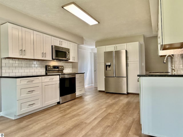7160 Cherry Ave, Kewadin, MI 49648 - kitchen featuring appliances with stainless steel finishes, backsplash, white cabinets, and light wood finished floors
