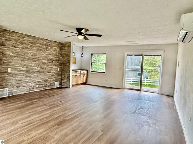 7160 Cherry Ave, Kewadin, MI 49648 - unfurnished living room with a textured ceiling, ceiling fan, a wall mounted AC, and wood finished floors