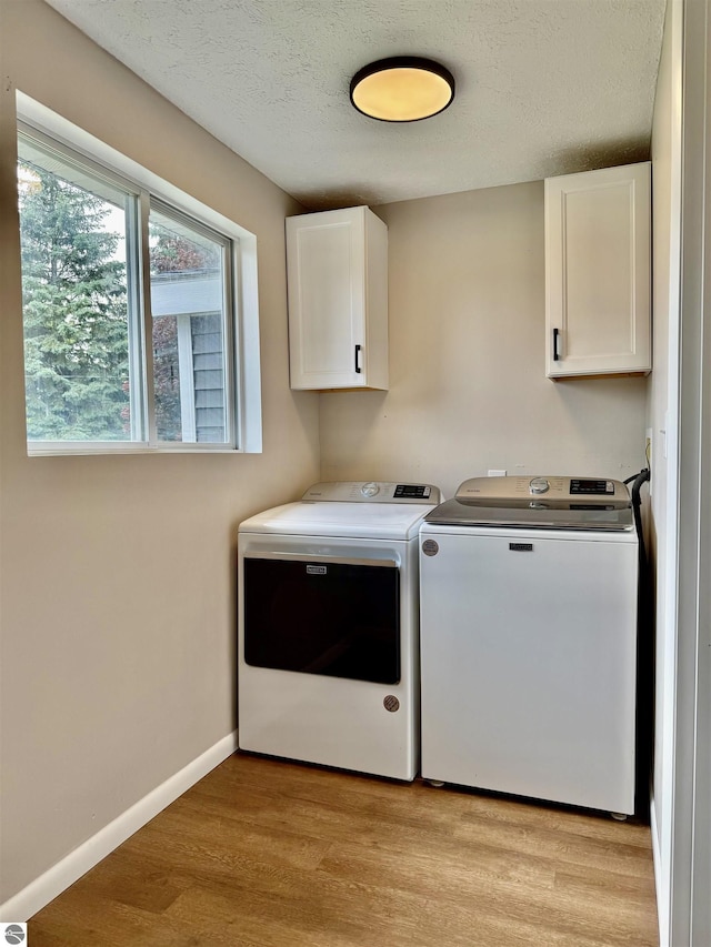 7160 Cherry Ave, Kewadin, MI 49648 - laundry area with cabinet space, independent washer and dryer, light wood-type flooring, and a textured ceiling
