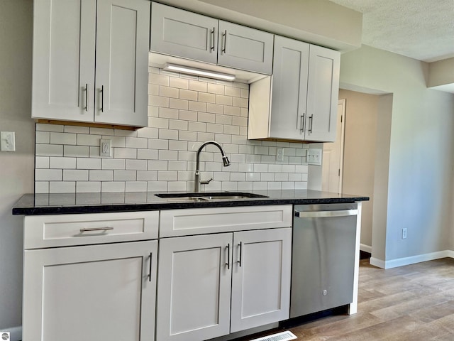 7160 Cherry Ave, Kewadin, MI 49648 - kitchen featuring stainless steel dishwasher, light wood-style floors, tasteful backsplash, white cabinetry, and dark stone countertops