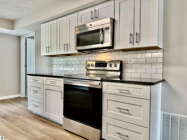 7160 Cherry Ave, Kewadin, MI 49648 - kitchen with appliances with stainless steel finishes, light wood-style floors, backsplash, a textured ceiling, and white cabinets