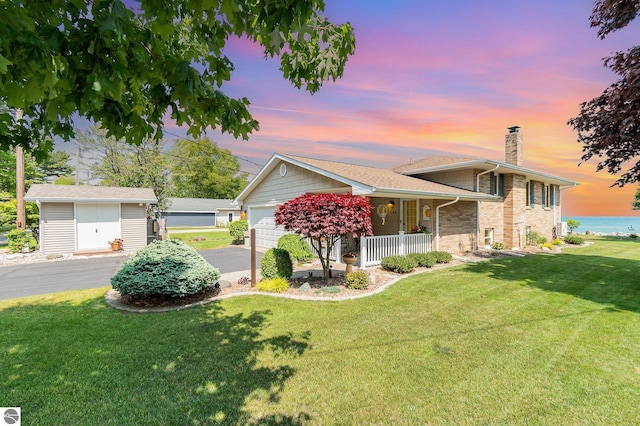 589 Pine Ln, East Tawas, MI 48730 - split level home featuring covered porch, a chimney, a front lawn, and a water view