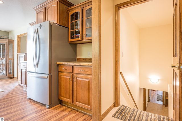 6375 S Isabella Rd, Shepherd, MI 48883 - kitchen with freestanding refrigerator, light wood finished floors, brown cabinets, glass insert cabinets, and light countertops