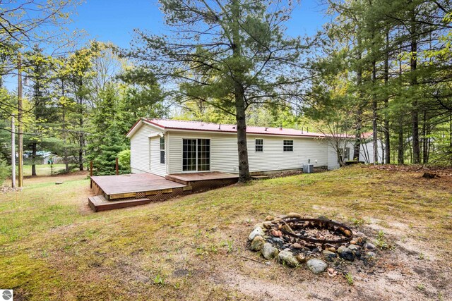 11748 NE Franklin St, Kalkaska, MI 49646 - rear view of house with a fire pit, a wooden deck, a metal roof, and a lawn
