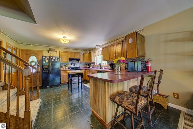 3721 W 18th Rd, Mesick, MI 49668 - kitchen with black appliances, a peninsula, under cabinet range hood, brown cabinetry, and tasteful backsplash