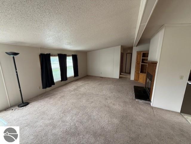 7372 Clans St, Alma, MI 48801 - unfurnished living room featuring light colored carpet, a textured ceiling, and a glass covered fireplace
